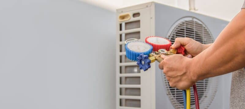 A technician using HVAC gauges to check refrigerant levels on an outdoor AC unit