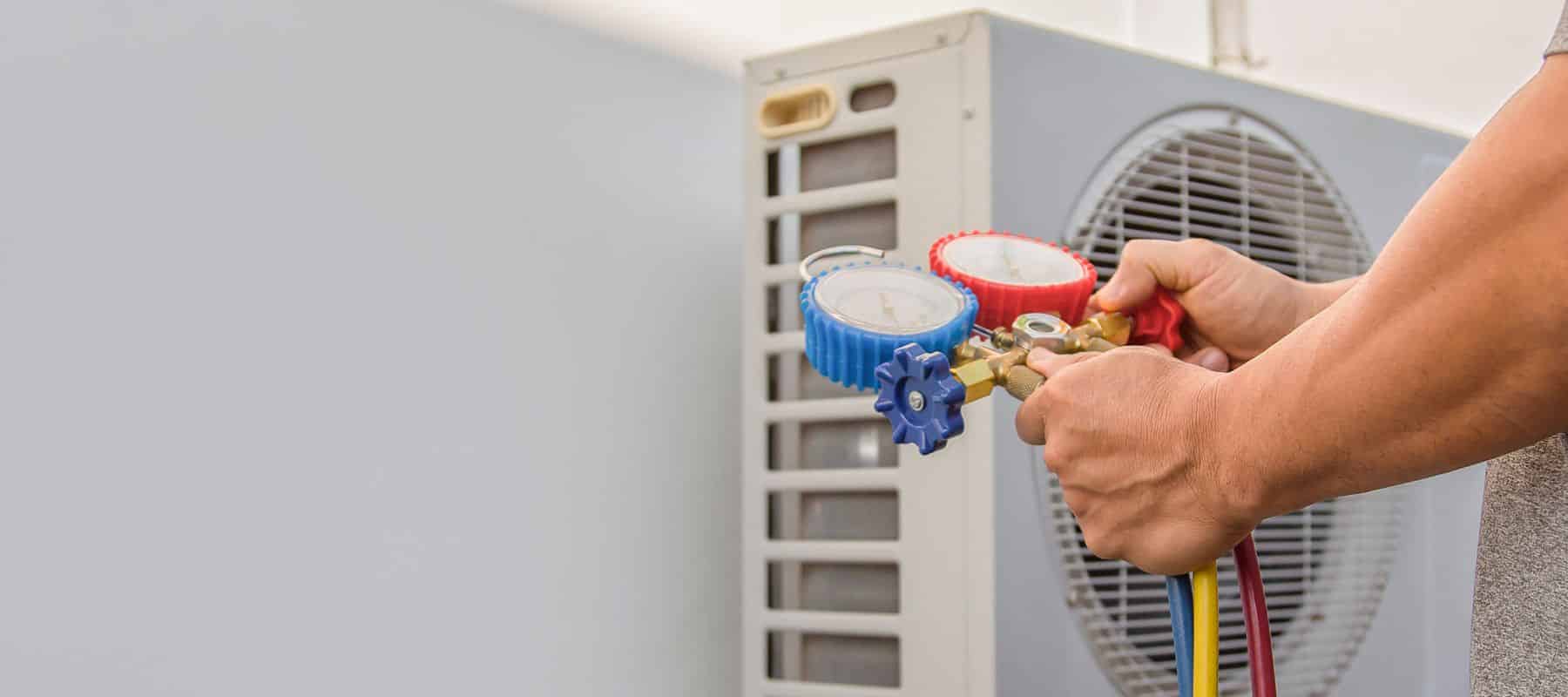 A technician using HVAC gauges to check refrigerant levels on an outdoor AC unit
